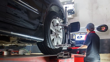 car undergoing a two wheel alignment service with technician and computer screen in background showing adjustments